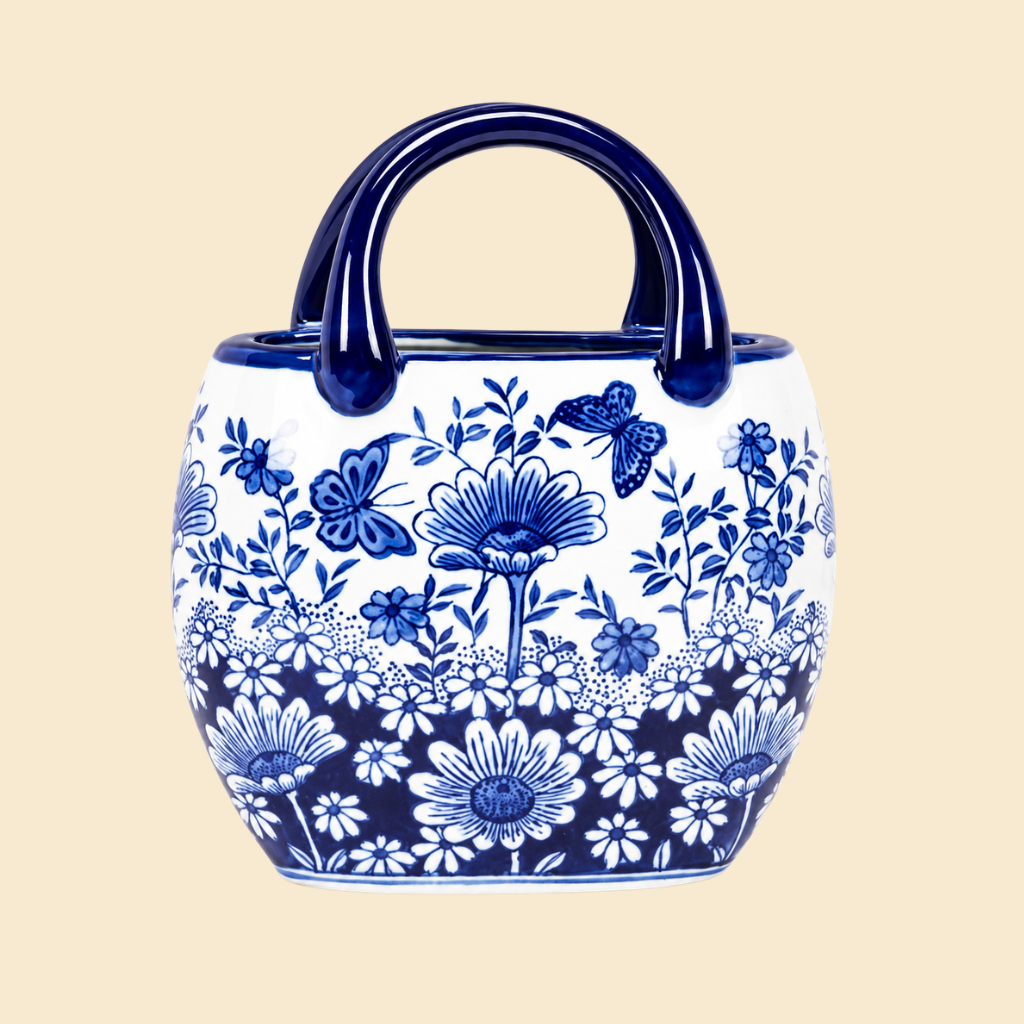 A ceramic planter pot with a rounded body, two dark blue handles, and a blue and white floral pattern, shown against a solid light beige background.