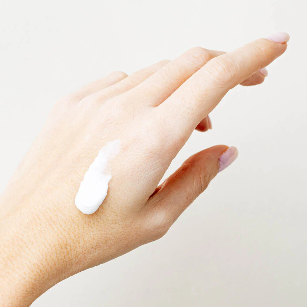 Hand with a small amount of cream on the back, against a light background