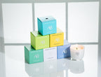 Set of colorful boxes with 'AB' branding and a lit candle on a reflective surface.