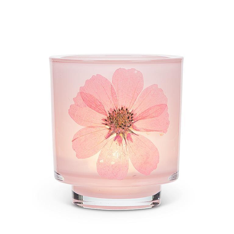 A pink glass jar candle with a large pressed pink flower embedded in the front, set against a plain white background.
