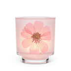 A pink glass jar candle with a large pressed pink flower embedded in the front, set against a plain white background.