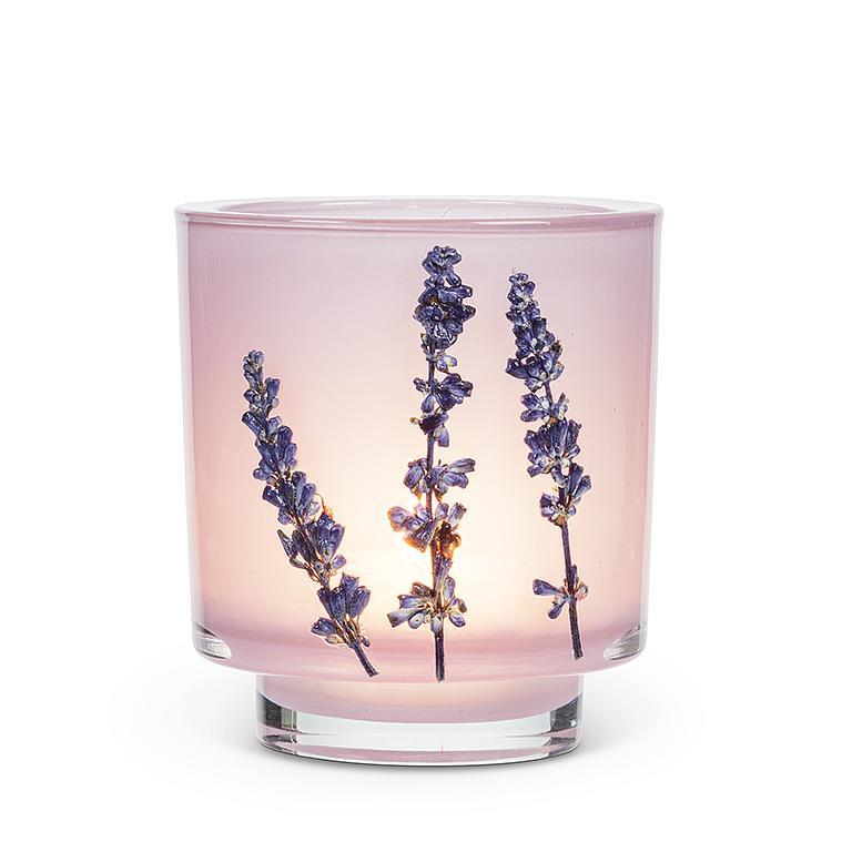 A pink glass candle holder with dried lavender sprigs inside, set against a plain white background.