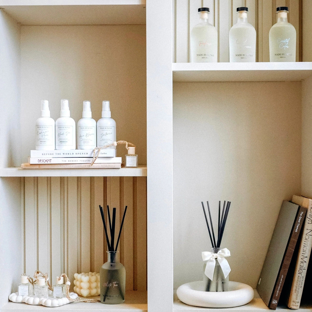 A styled interior shelf display featuring white diffusers, reed diffuser bottles, books, and small decorative objects arranged in built-in shelving.