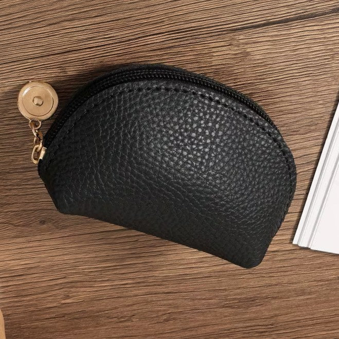 Black leather coin purse with gold zipper pull on a wooden surface