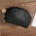 Black leather coin purse with gold zipper pull on a wooden surface