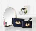 Navy makeup bags with eye designs on a vanity table with mirrors and decor.