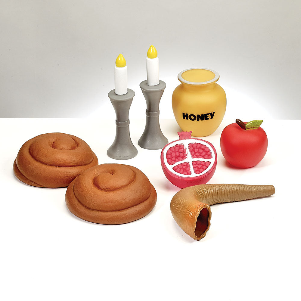 Set of Rosh Hashana food replicas including challah, candles, honey jar, pomegranate, and apple on a white background.