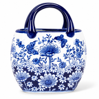 A ceramic bucket-style vase with a glossy blue handle, decorated with a blue and white floral and butterfly pattern on a white background.