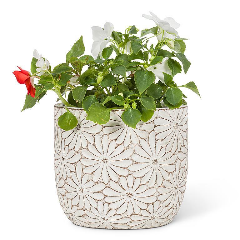Decorative white ceramic planter with floral patterns containing green plants and red flowers on a white background