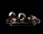 Three purple glass vases on a clear acrylic stand against a black background