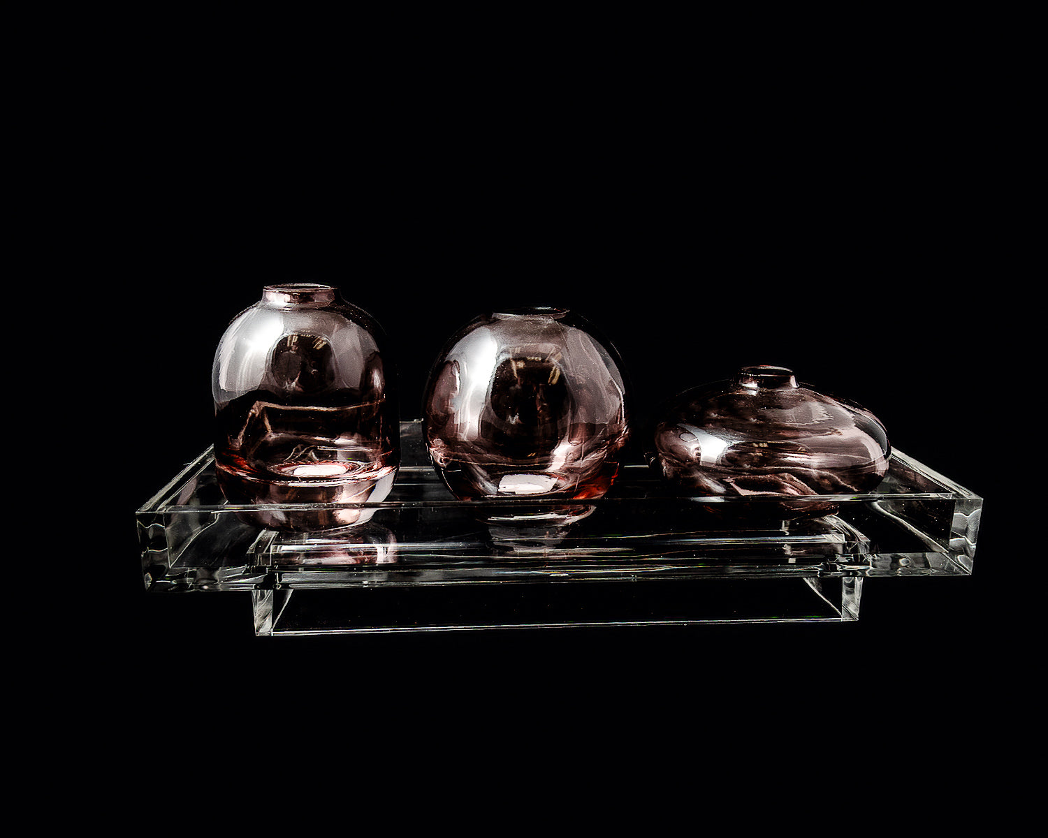 Three purple glass vases on a clear acrylic stand against a black background