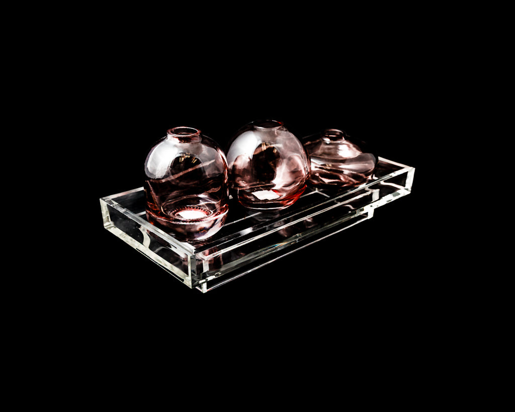 Three round glass vases on a clear rectangular tray against a black background