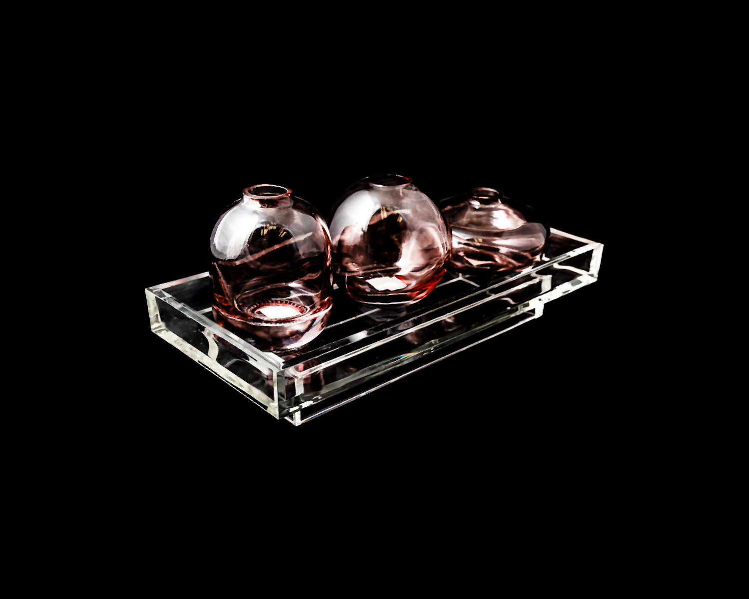 Three round glass vases on a clear rectangular tray against a black background