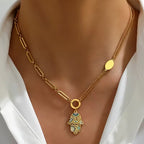 Gold necklace with a hamsa hand pendant on a model wearing a white shirt.