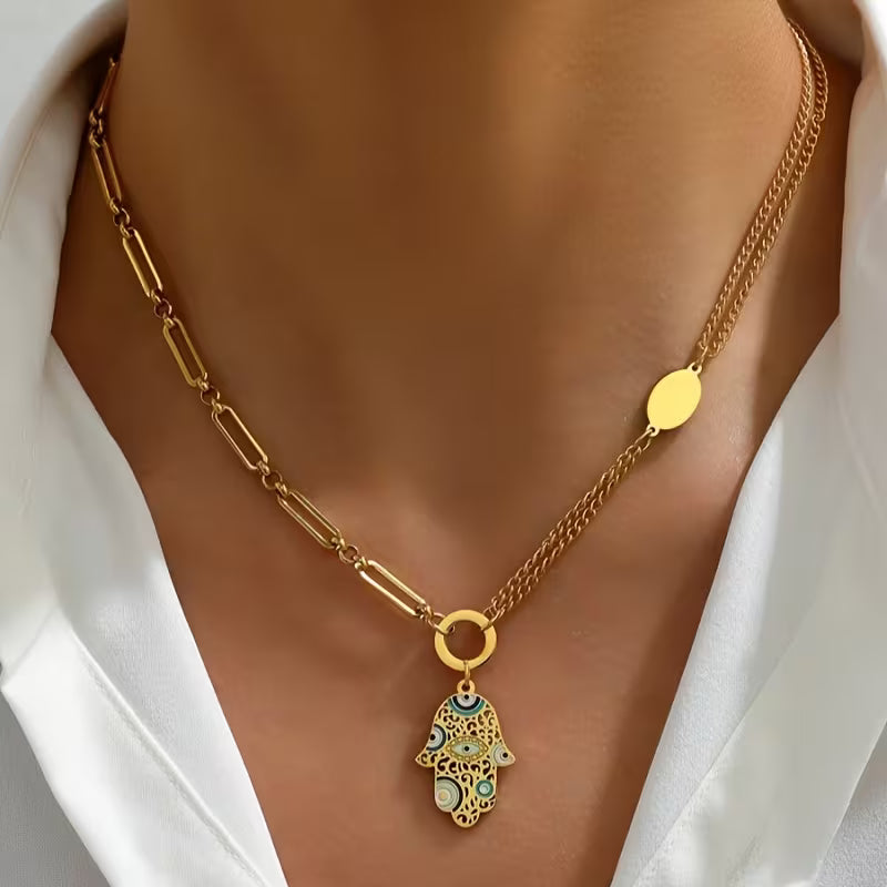 Gold necklace with a hamsa hand pendant on a model wearing a white shirt.