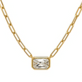 A gold paperclip chain necklace with a rectangular bezel-set clear gemstone pendant, shown against a plain white background.