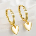 Gold hoop earrings with heart pendants on a light background