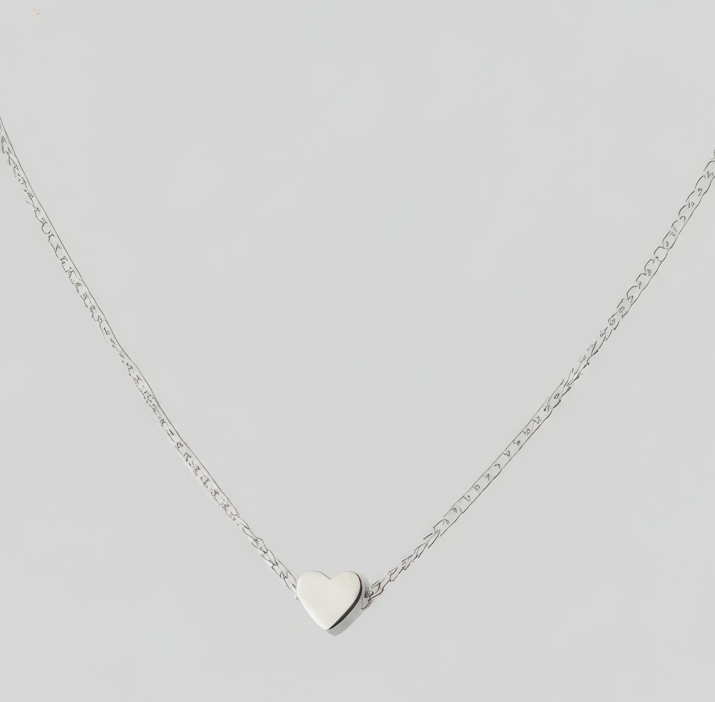 A delicate silver chain necklace with a small, polished silver heart pendant, displayed against a solid light gray background.
