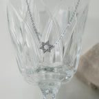 A silver pendant with the Star of David charm, hanging in front of a glass goblet.