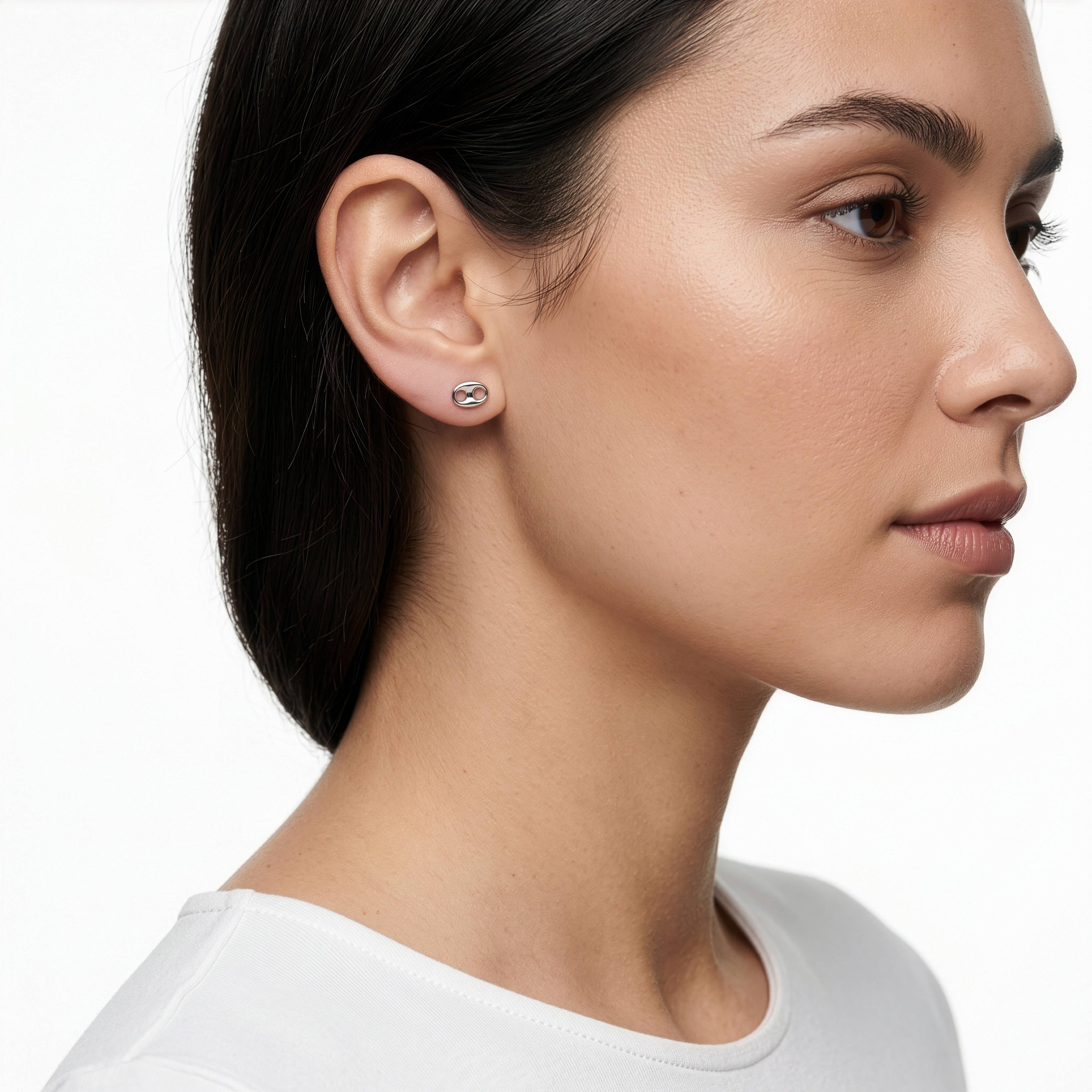 A close-up side profile of a woman wearing a small silver stud earring with a clear gemstone, set against a clean white background.