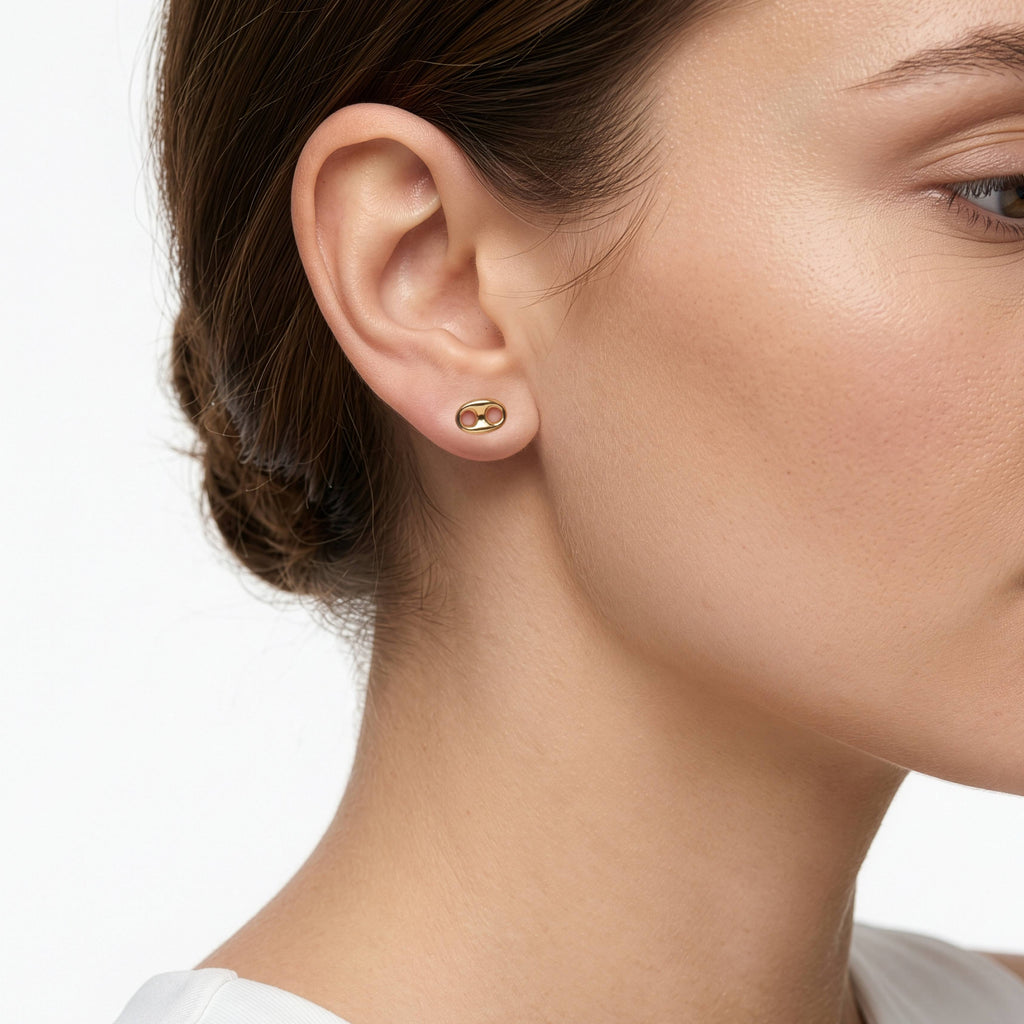 A close-up of a woman's ear wearing a small gold stud earring with a double-ring design, set against a clean white background.