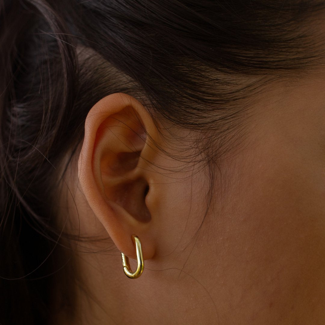 A close-up of a person's ear wearing a small gold huggie hoop earring.