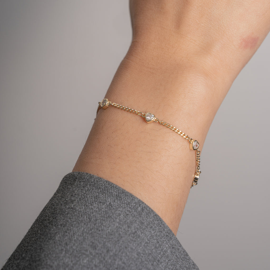 A delicate gold chain bracelet with small clear crystal accents, shown worn on a person's wrist against a soft gray background.