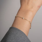 A delicate gold chain bracelet with small clear crystal accents, shown worn on a person's wrist against a soft gray background.
