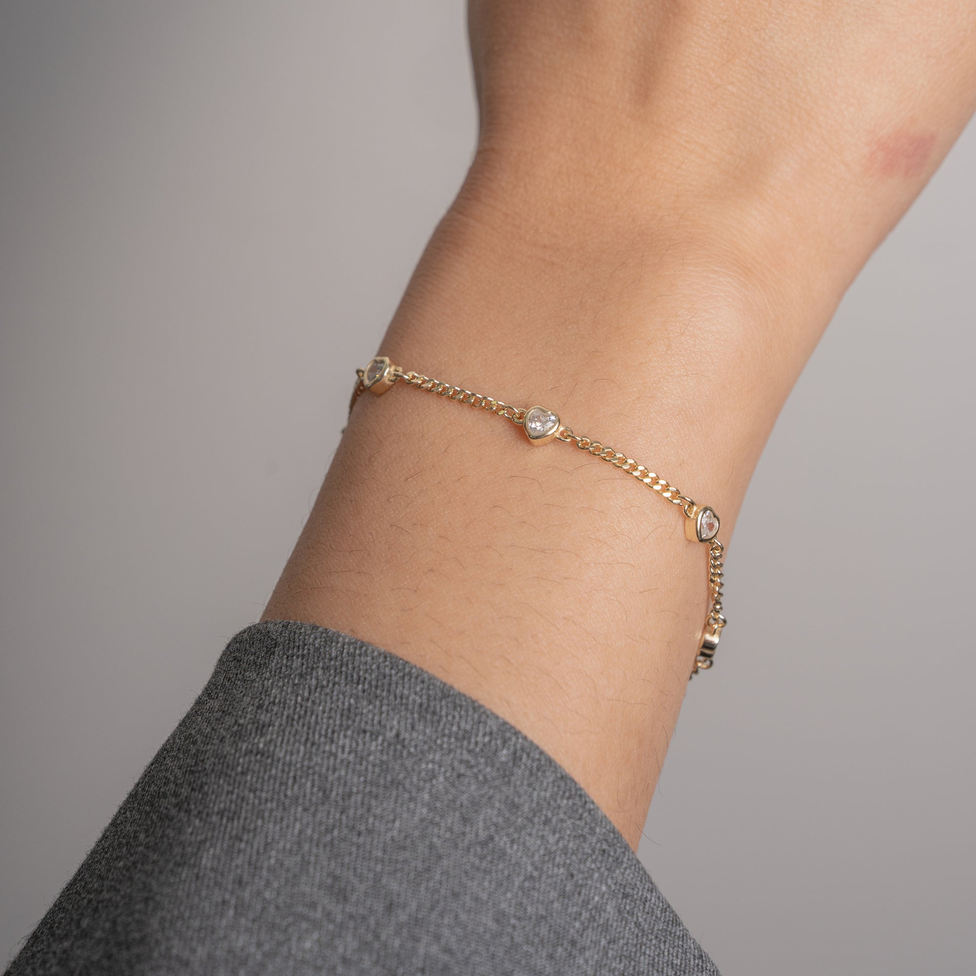A delicate gold chain bracelet with small clear crystal accents, shown worn on a person's wrist against a soft gray background.