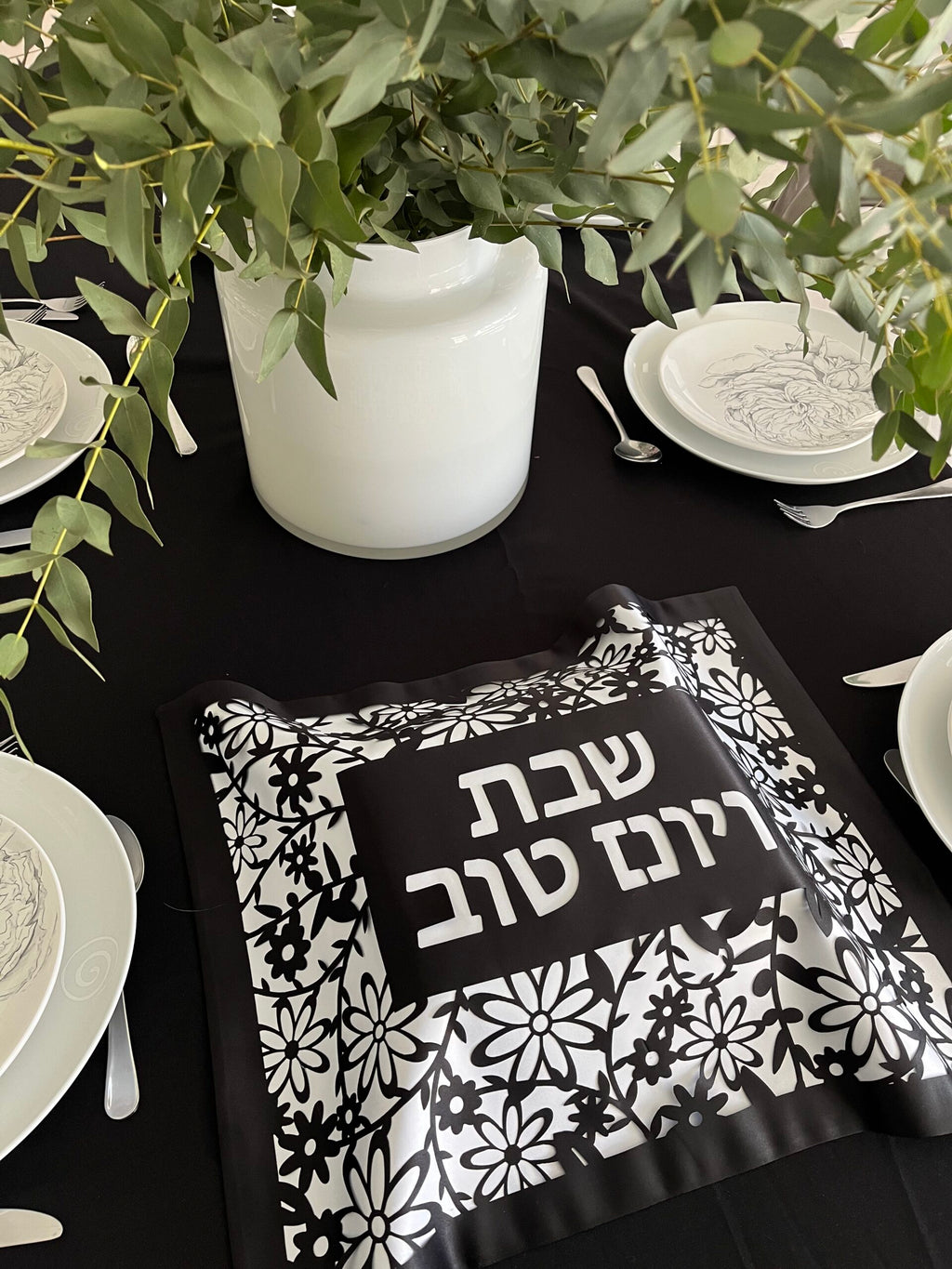 Table setting with black and white patterned napkin and Hebrew text on a black tablecloth.