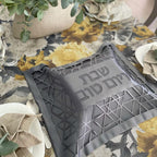 Gray decorative mat with Hebrew text on a floral tablecloth