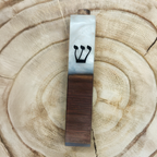 A mezuzah case made of white marble on the top half and dark brown wood grain on the bottom half, featuring a black Hebrew letter Shin, displayed on a circular wood slice background.