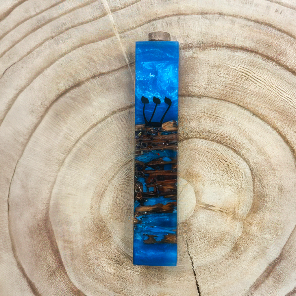 A rectangular mezuzah with a blue and brown wood-grain pattern, displayed on a natural wood slice background.