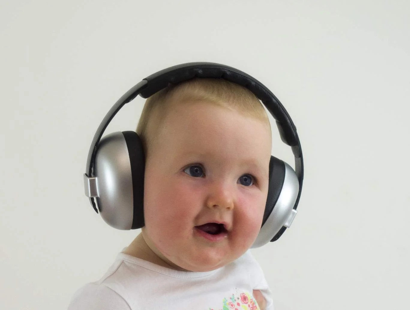 A baby wearing large silver and black over-ear headphones against a plain light background.