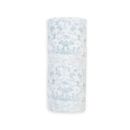 A rolled-up white muslin swaddle blanket or baby wrap, featuring a light blue toile de Jouy pattern of figures and trees, shown against a plain white background.