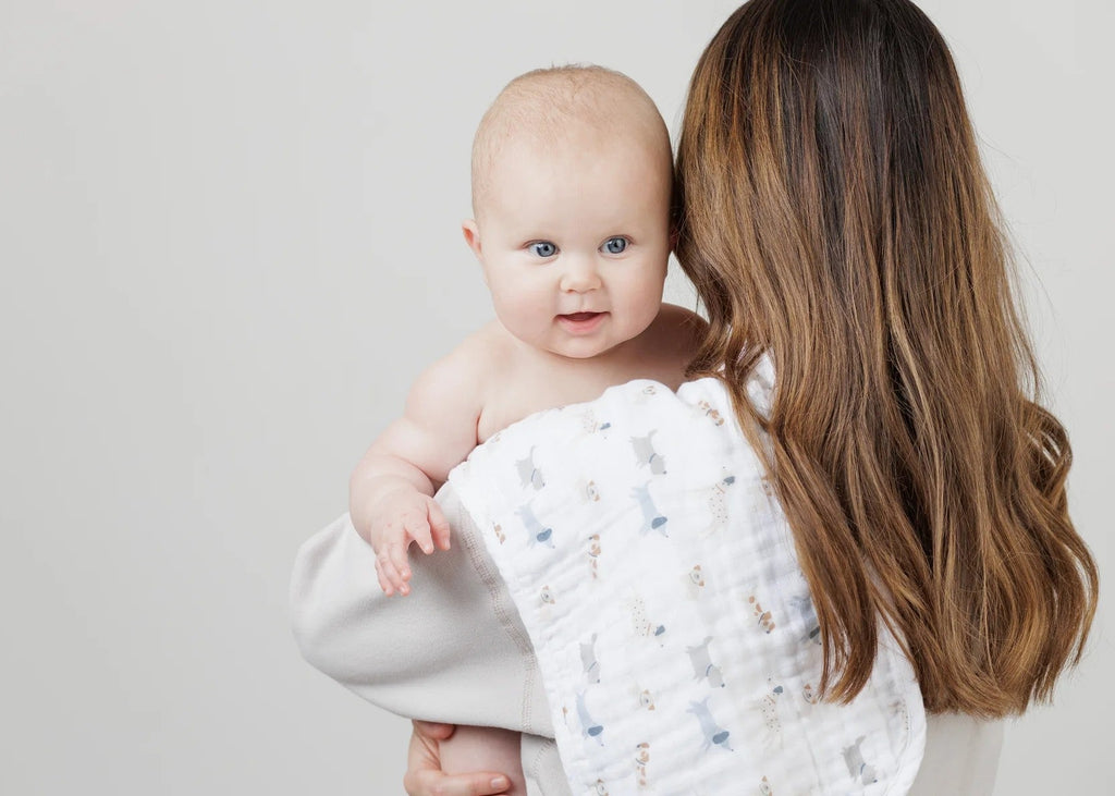 Woman holding a baby wrapped in a white blanket with blue patterns against a plain background