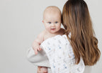 Woman holding a baby wrapped in a white blanket with blue patterns against a plain background