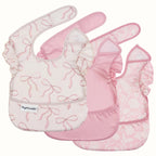 Three pink baby bibs with ruffled edges, overlapping on a light cream background. The bibs feature different prints: one with pink bow motifs on a white base, one solid light pink, and one with a pale pink floral pattern.