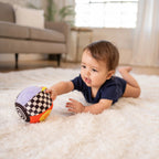 Baby playing with a colorful ball on a carpeted floor in a living room.