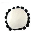 Round white pillow with black pom-pom trim on a white background