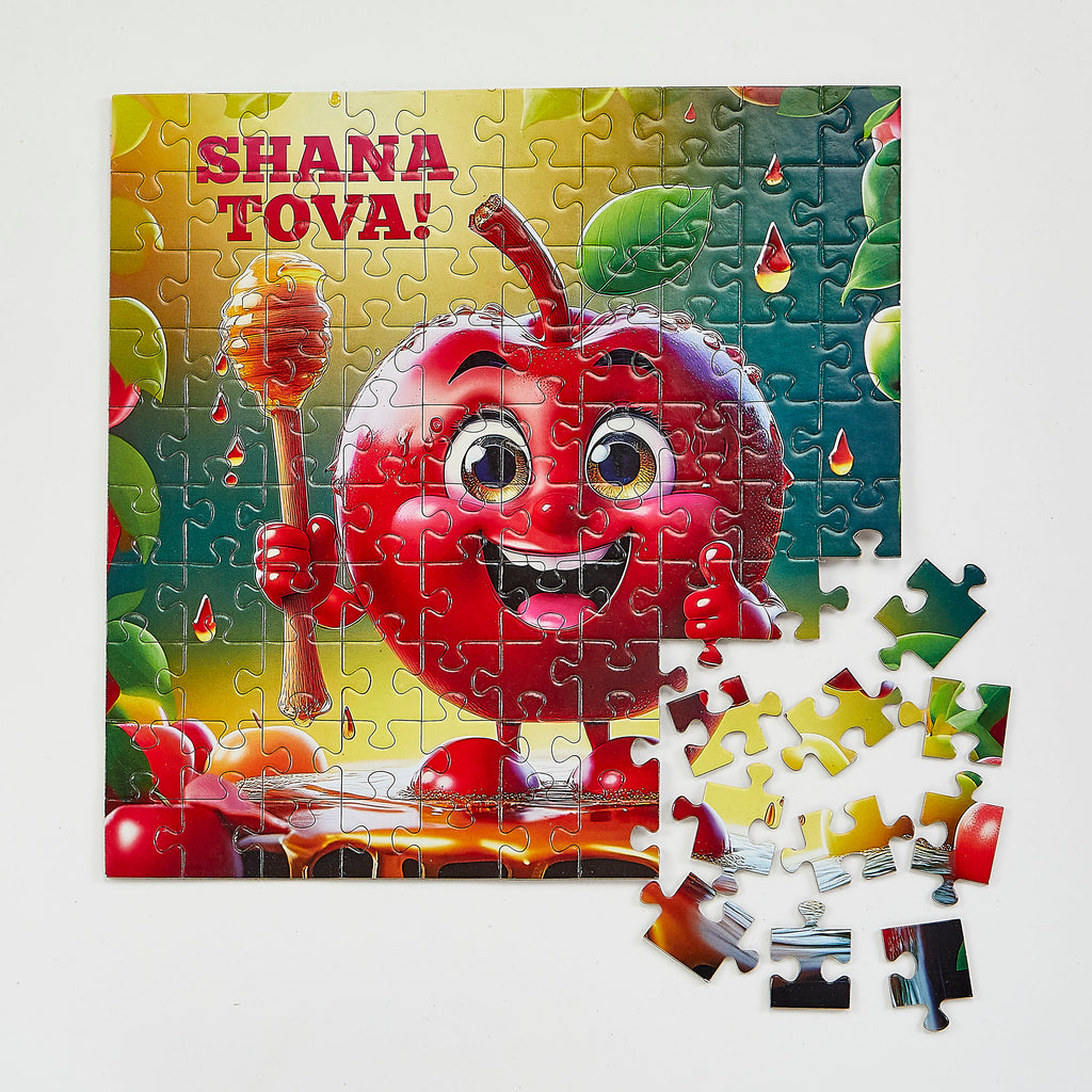 A colorful children's jigsaw puzzle featuring a smiling red apple character holding a honey dipper, with the text 'SHANA TOVA!' at the top. The puzzle is shown assembled with several loose pieces placed in front on a light neutral background.