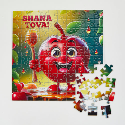 A colorful children's jigsaw puzzle featuring a smiling red apple character holding a honey dipper, with the text 'SHANA TOVA!' at the top. The puzzle is shown assembled with several loose pieces placed in front on a light neutral background.