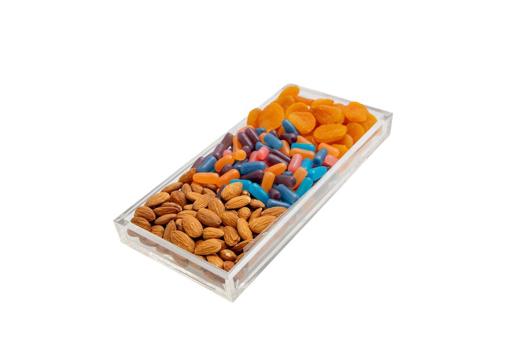 A clear rectangular plastic tray filled with mixed nuts and colorful capsules, photographed on a plain white background.
