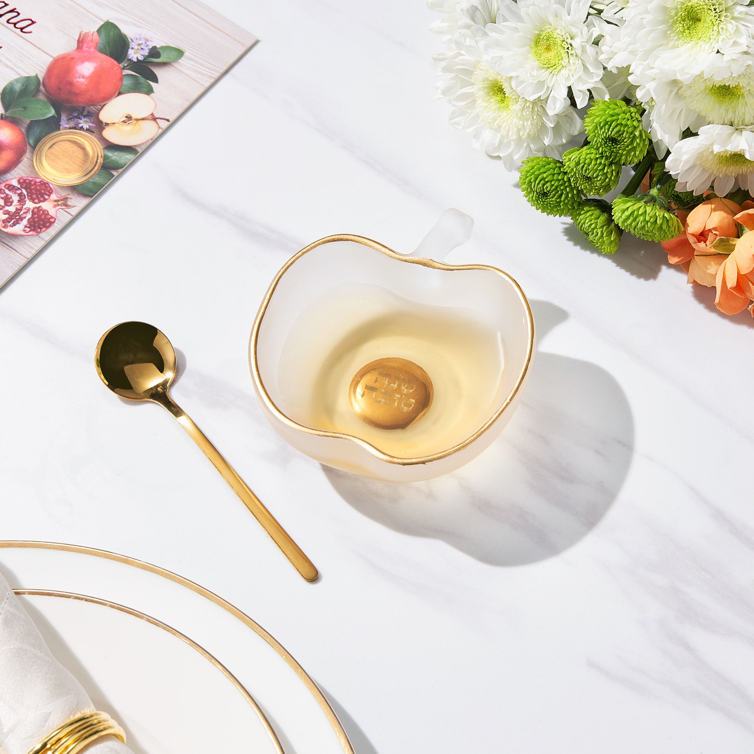 Decorative bowl with gold interior, spoon, and flowers on a white surface