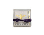 A square clear acrylic gift box containing a white napkin with a gold bee design, a gold honeycomb border, and a dark purple satin ribbon tied in a bow, set against a plain white background.
