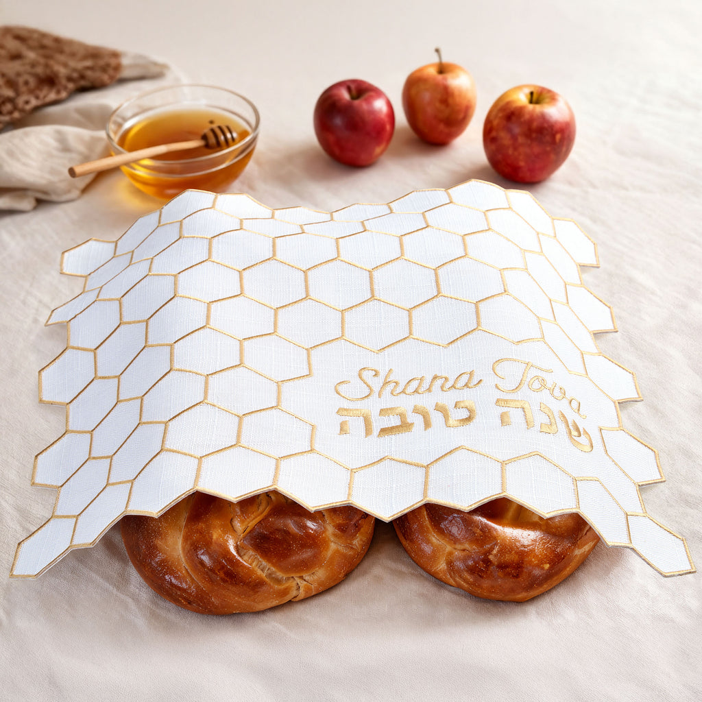 Honeycomb-patterned challah cover with 'Shana Tova' text, apples, and honey dipper on a light background.