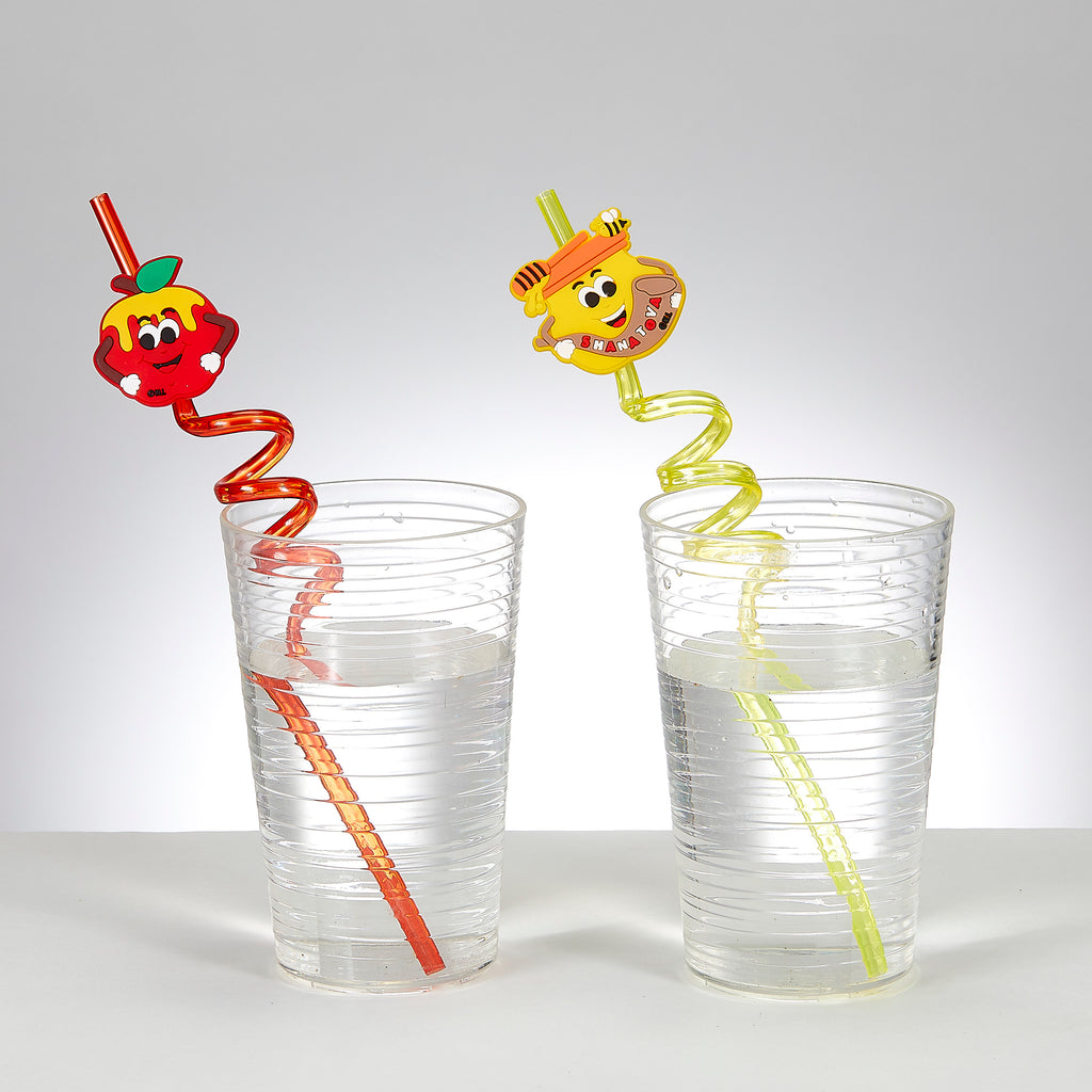 Two novelty spiral straws with cartoon fruit and honey characters, shown inserted into clear plastic cups filled with water on a white surface against a light gray background.
