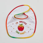A white baby bib with a rainbow-colored stitched border and an embroidered design featuring a red apple with honey dripping from it, surrounded by the text 'I'M SWEETER THAN HONEY!'.