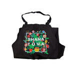 A black apron with a colorful floral border and the words 'SHANA TOVA' printed in the center, shown against a plain white background.