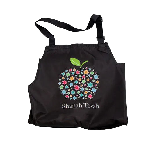 A black fabric bib-style apron featuring a colourful floral apple graphic and the text 'Shanah Tovah' printed on the front, shown against a plain white background.